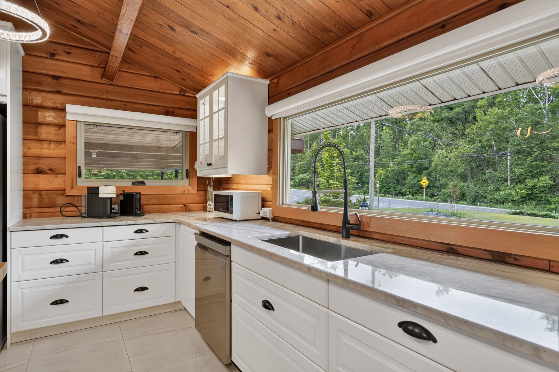 Kitchen with white cabinets, a long sink window, and warm wood walls and ceiling.