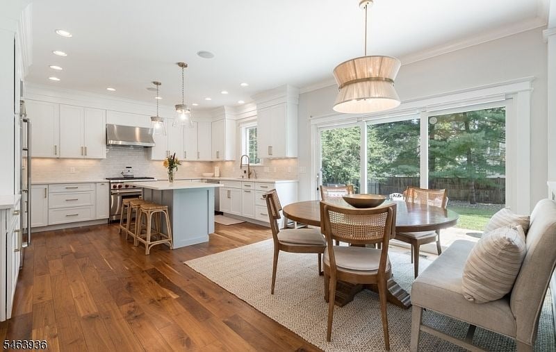 Open kitchen and dining area with a pale blue island, hardwood floors, and glass doors overlooking trees.