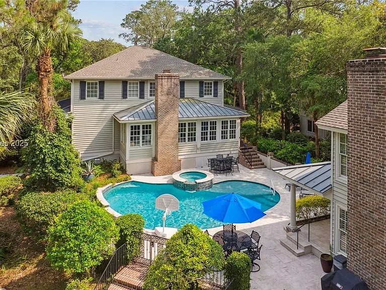 Backyard pool and raised spa between homes, with blue umbrellas and a brick chimney.