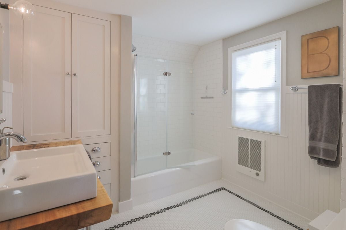 White bathroom with a glass-enclosed tub, paneled vanity, and wood countertop.