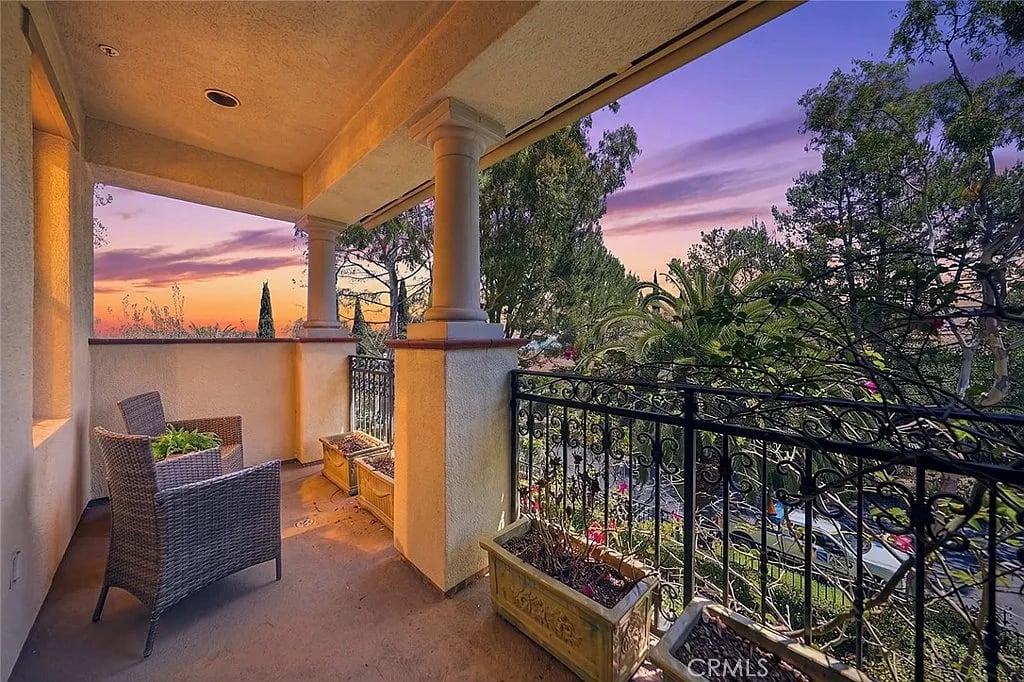 Covered balcony with wicker chairs and planters overlooking trees at sunset.