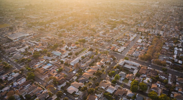 Aerial view of a suburban neighborhood with tree-lined streets in warm evening light.