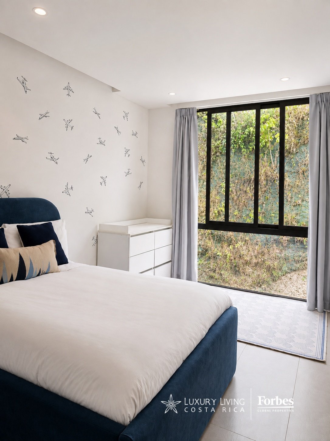 Furnished bedroom with a navy bed, airplane wall decorations, and a large window overlooking greenery.