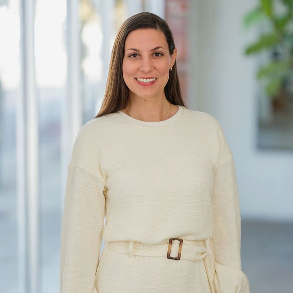 Nicole Norris smiles in a cream sweater and belted trousers.
