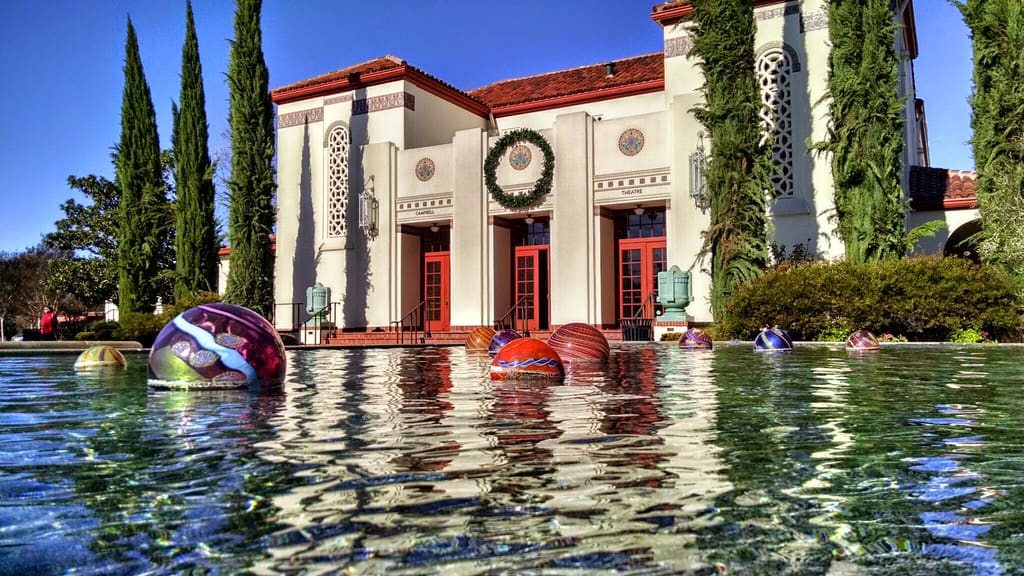 Campbell Theatre behind a reflecting pool with colorful floating spheres and tall cypress trees.