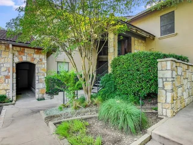 Stone and stucco courtyard entry to a ground-floor condo at Liberty Park Condominiums in West Lake Hills, Austin, Texas, with mature landscaping along the walkway.