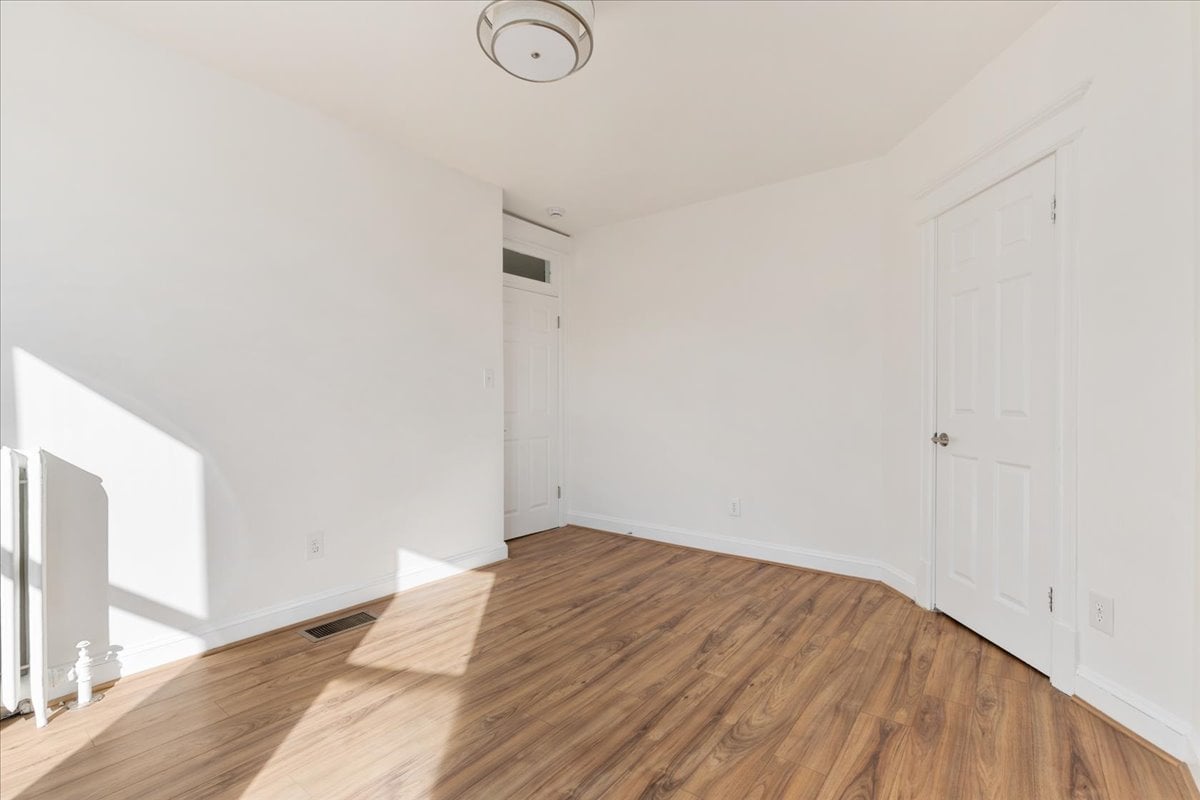 Empty room with warm wood flooring, white walls, and sunlight across the floor.