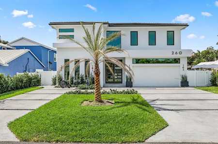 Modern white two-story home with a front lawn, palm tree, and wide driveway.
