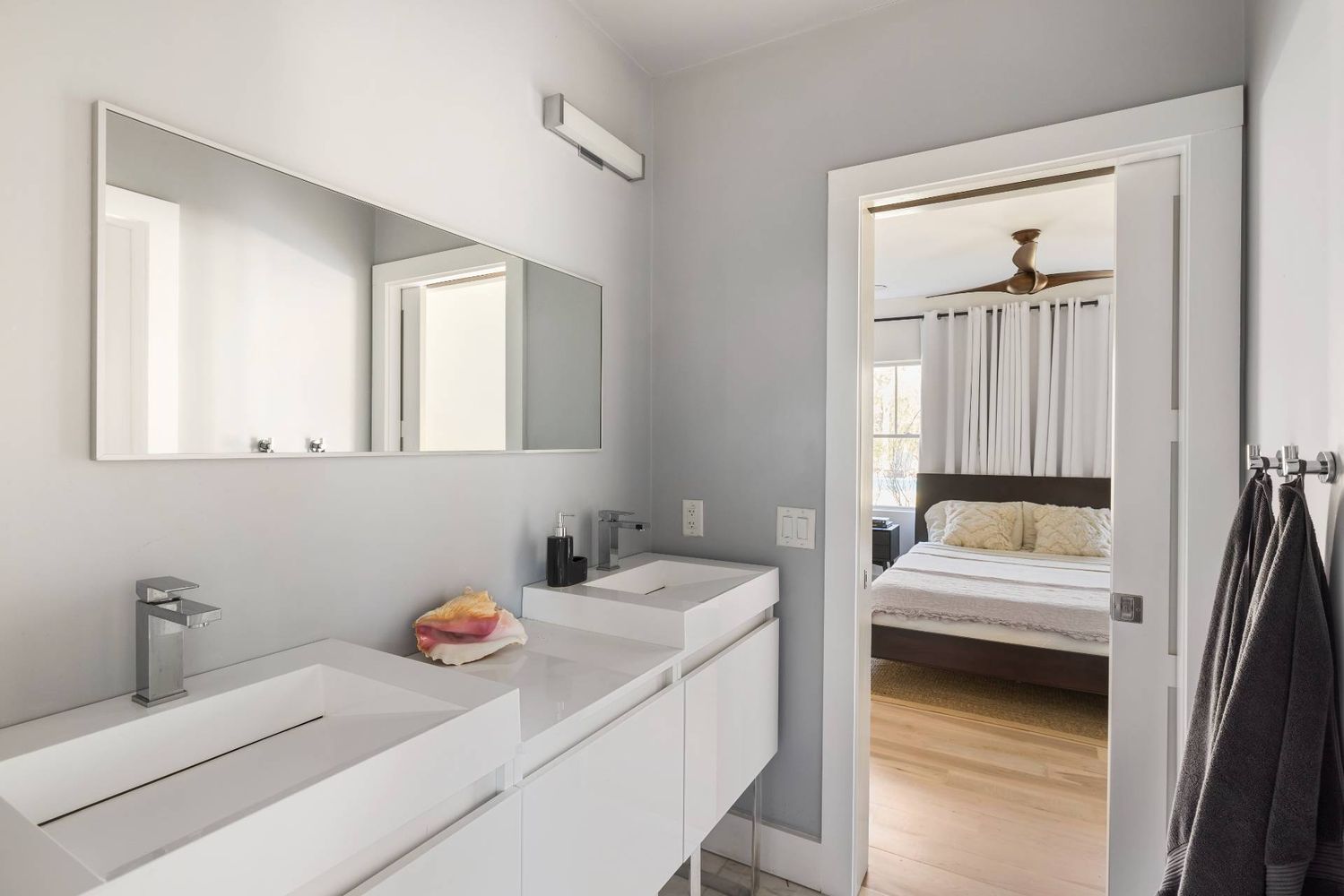 Bathroom with a double-sink vanity and a doorway looking into a bedroom.