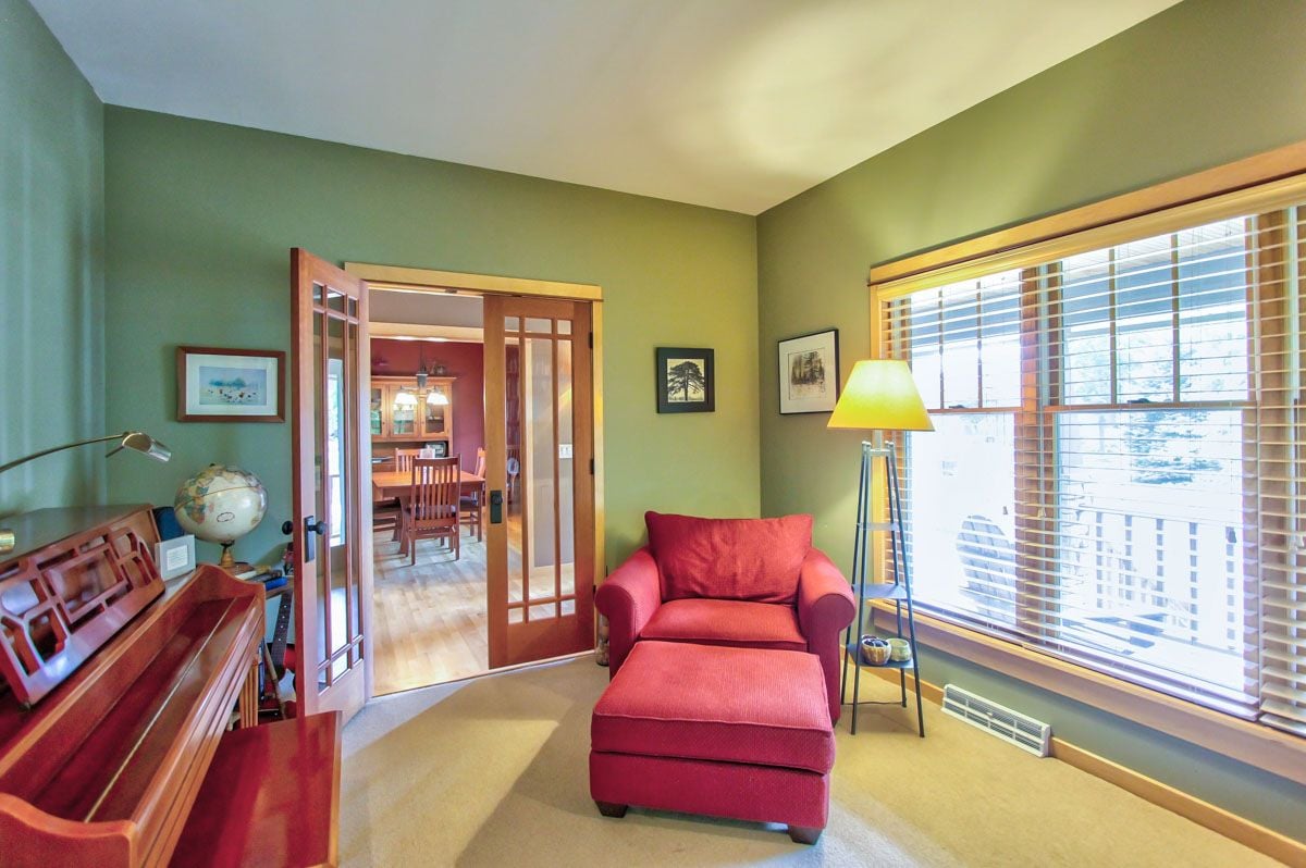 Living room with a red armchair and ottoman, upright piano, and French doors to the dining area.
