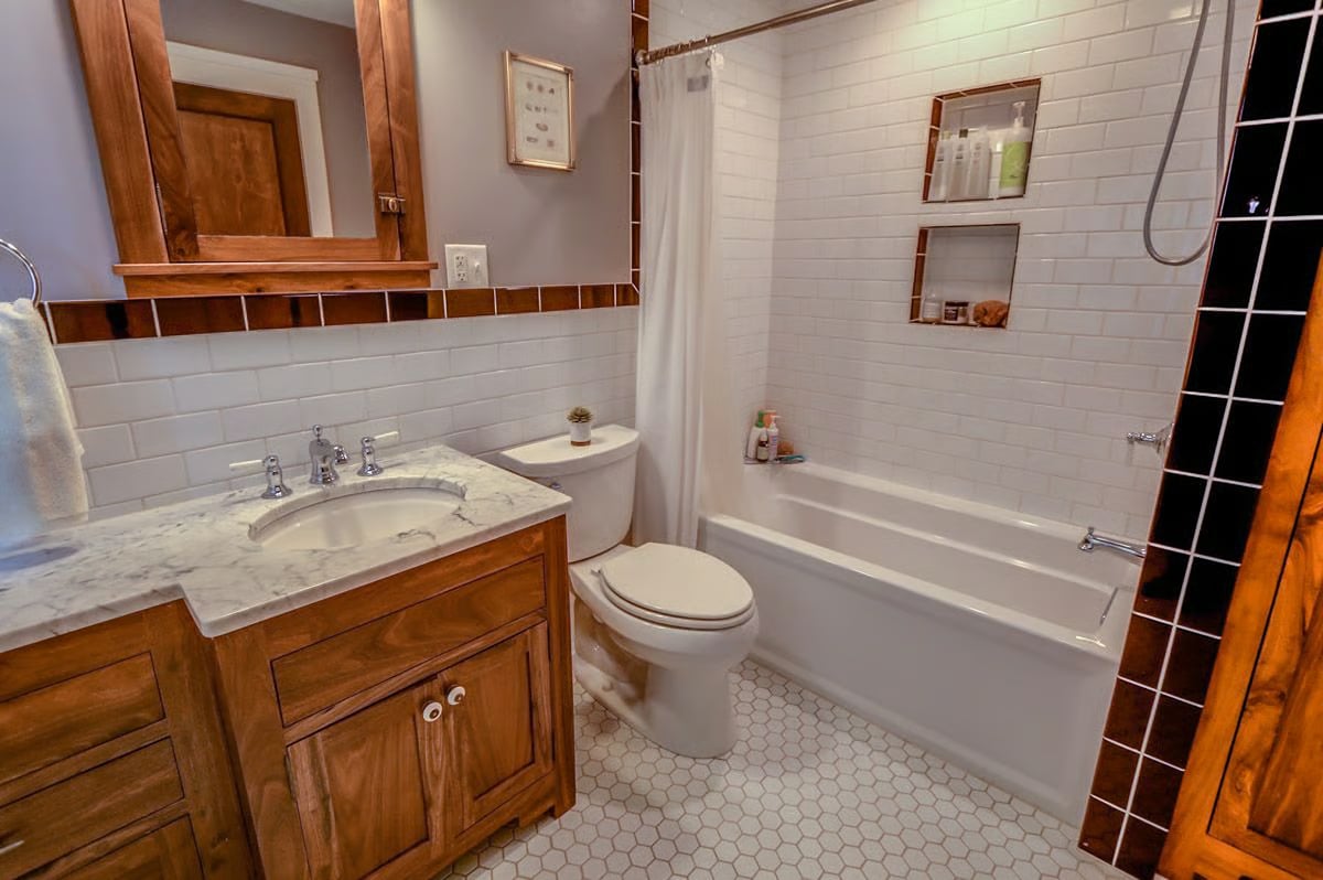 Bathroom with a wood vanity, marble countertop, white subway tile, and bathtub with shower.