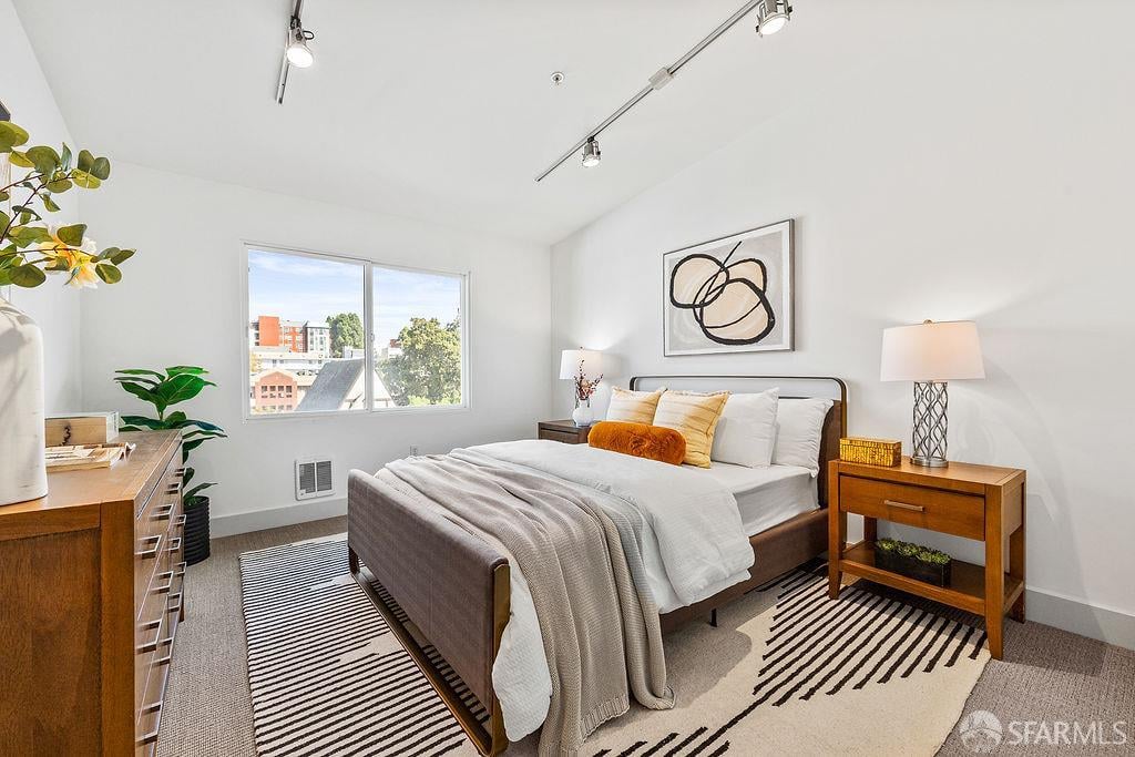 Staged bedroom with a large white bed, striped rugs, and a window overlooking nearby buildings.