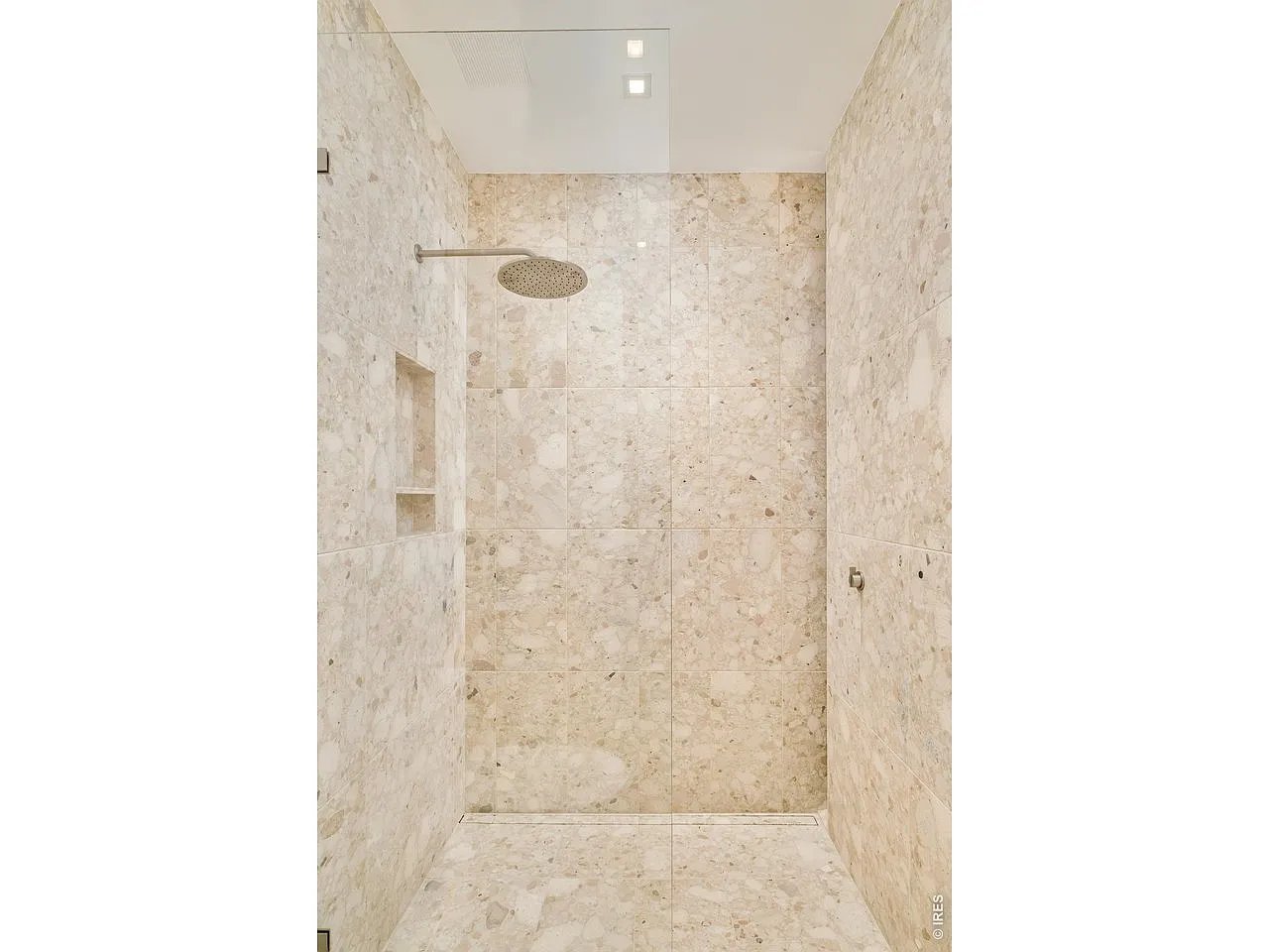 Walk-in shower with cream stone tile, a round rainfall showerhead, and a recessed niche.