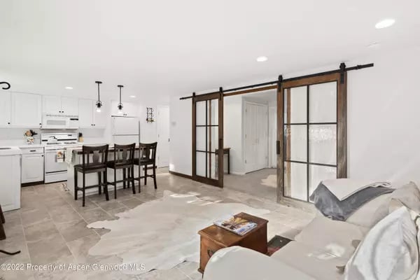 Open-plan Aspen condo with white kitchen, dining table, sliding barn doors, and a light sectional sofa.