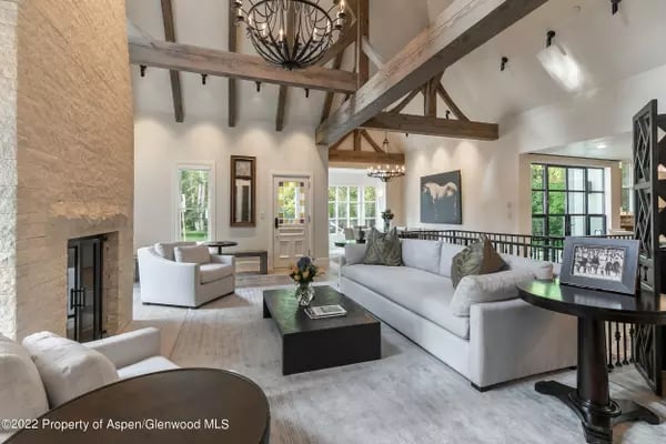 Living room with a stone fireplace, exposed timber beams, and large windows.