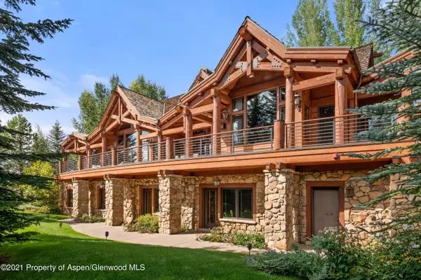 Multi-level timber-and-stone home with a long balcony and landscaped lawn.