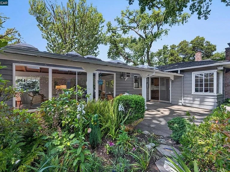 Gray single-story home with a covered patio, outdoor dining area, and leafy garden.