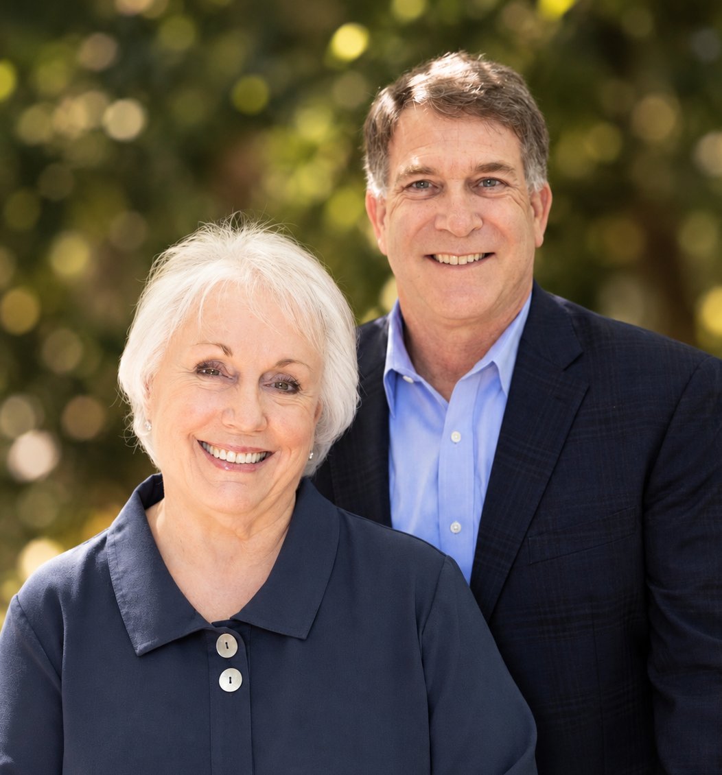 Two smiling real estate agents pose together outdoors against a leafy background.