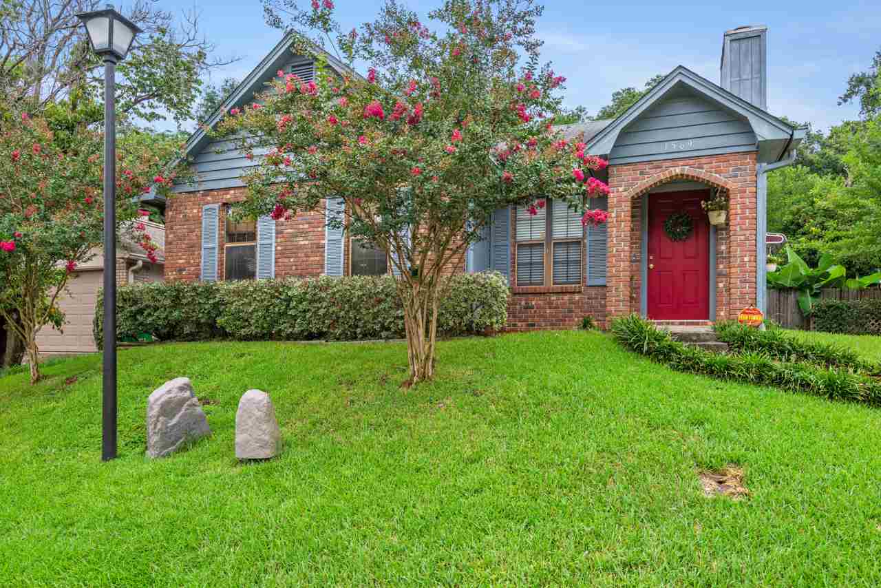 A brick house featuring a red door, surrounded by lush green grass.