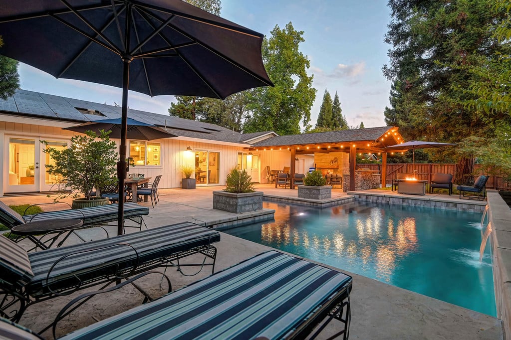 Backyard pool and patio with covered seating, string lights, and a glowing fire feature.