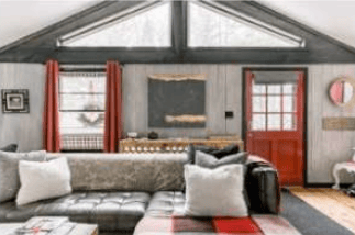 Living room with a dark sectional, fireplace, exposed timber beams, and red-trimmed windows.