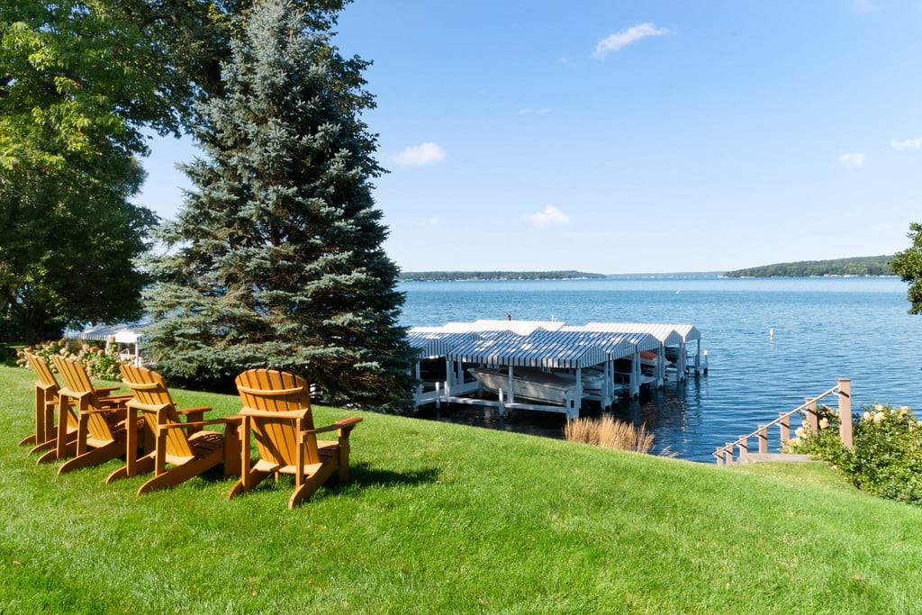 Adirondack chairs on a grassy lakeside lawn beside a covered boat dock.