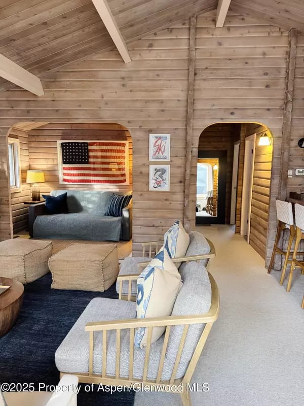 Wood-paneled living room with exposed beams, pale seating, and an American flag.