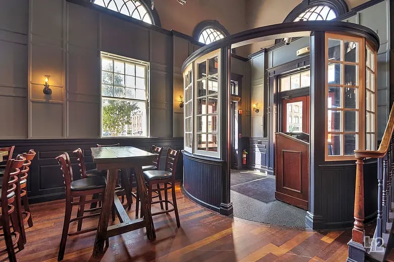 Dining area with dark wood paneling, small tables, arched windows, and a curved glass-paneled entry.