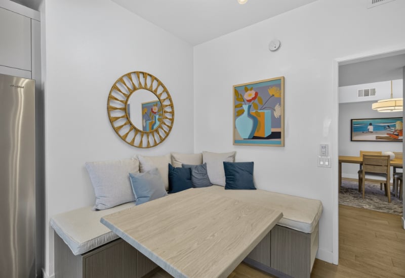 Dining nook with an L-shaped banquette, pale wood table, and blue cushions beside the kitchen.