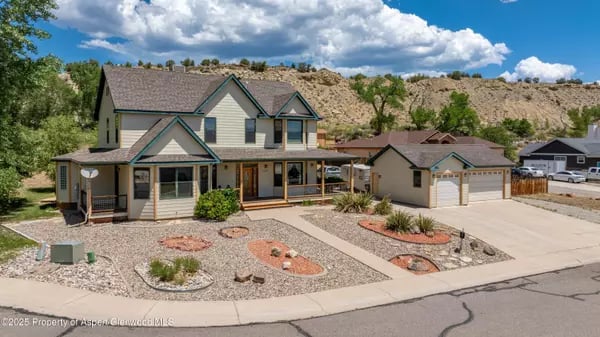 Two-story home with a covered porch, garage, and gravel landscaping beneath a rocky hillside.