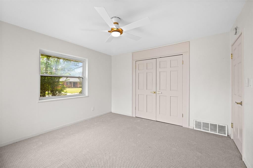 Empty bedroom with carpet, double closet doors, and a window overlooking a green lawn.