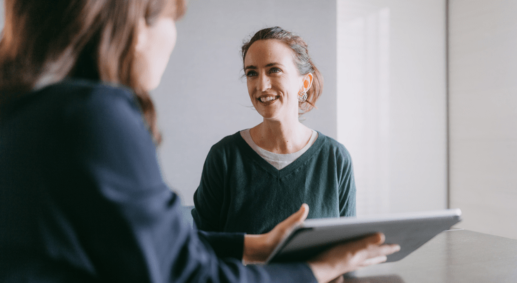 Two people sit across from each other in a meeting. One holds a tablet, while the other smiles warmly, creating a positive, collaborative atmosphere.