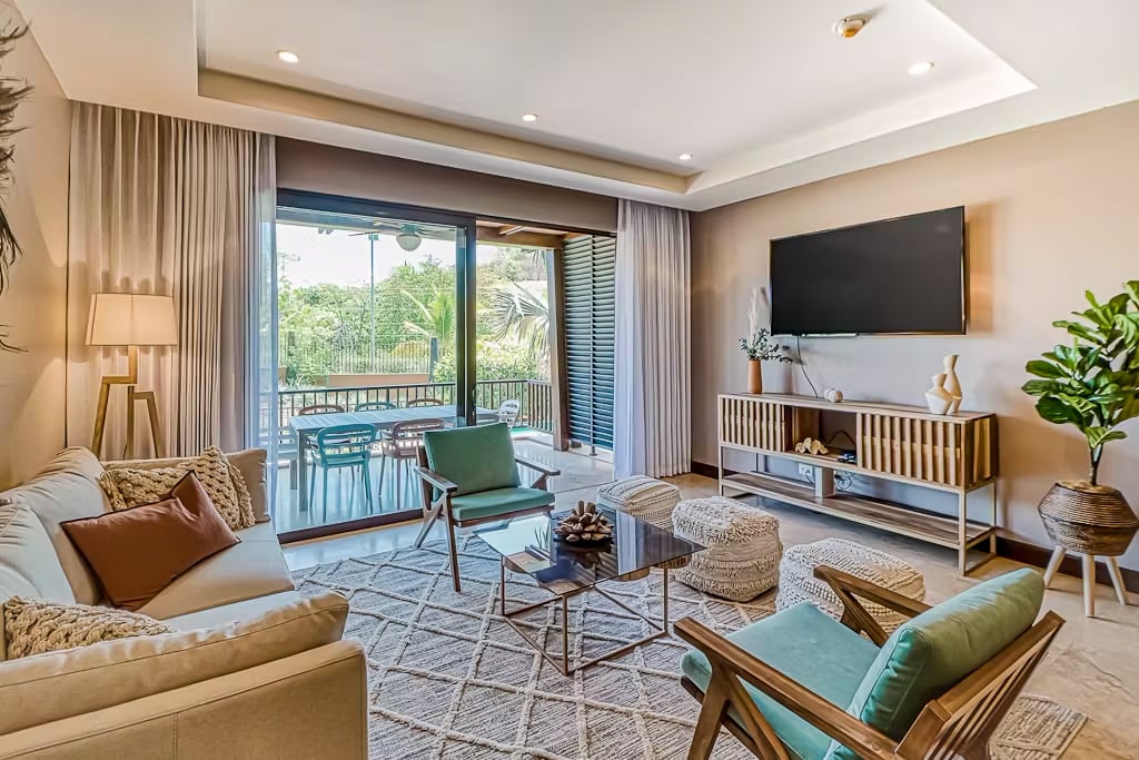 Furnished living room with teal chairs and sliding doors opening onto a leafy balcony.