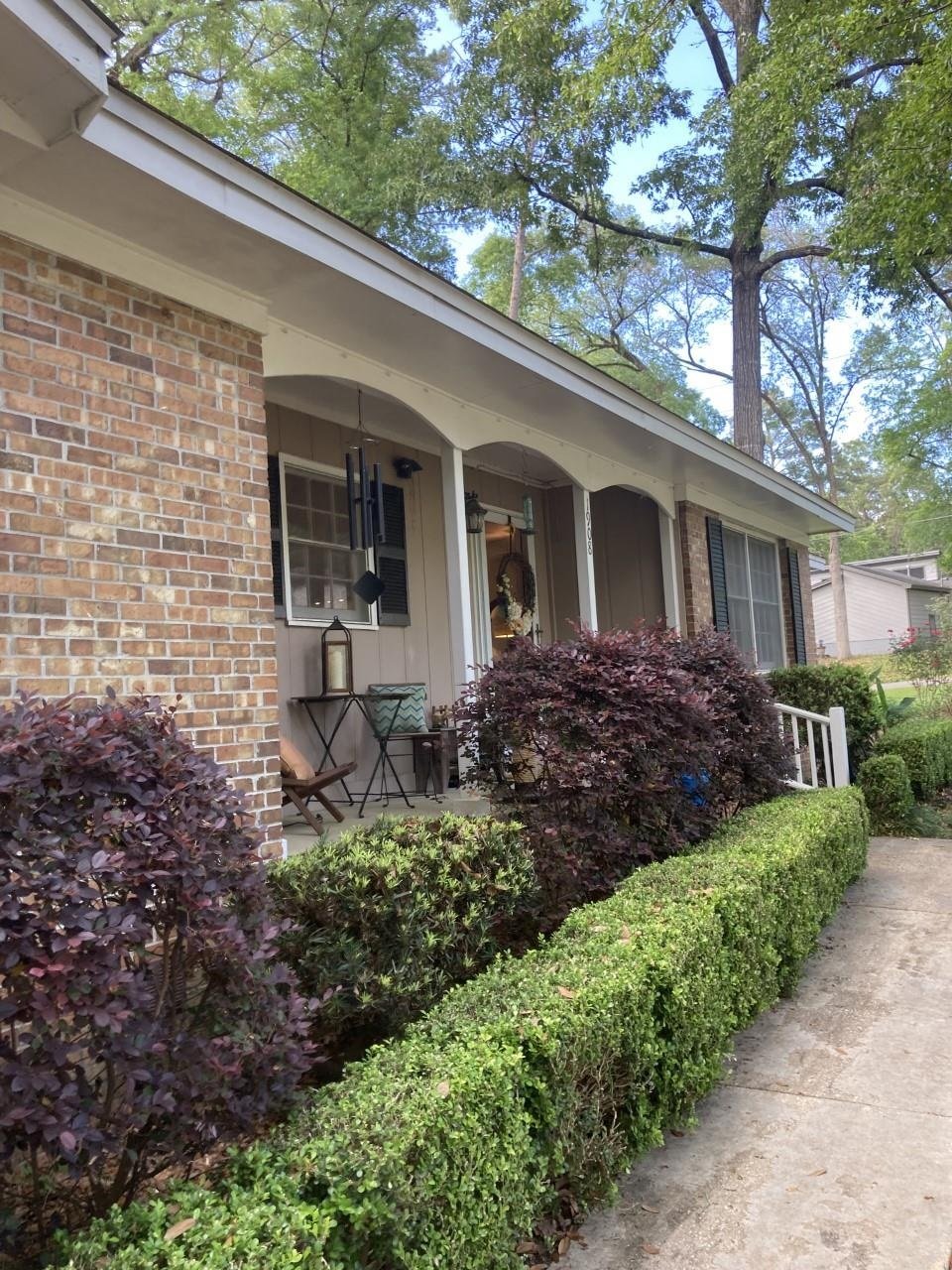 A brick home surrounded by lush bushes and shrubs in the front yard, showcasing a welcoming and well-maintained exterior.