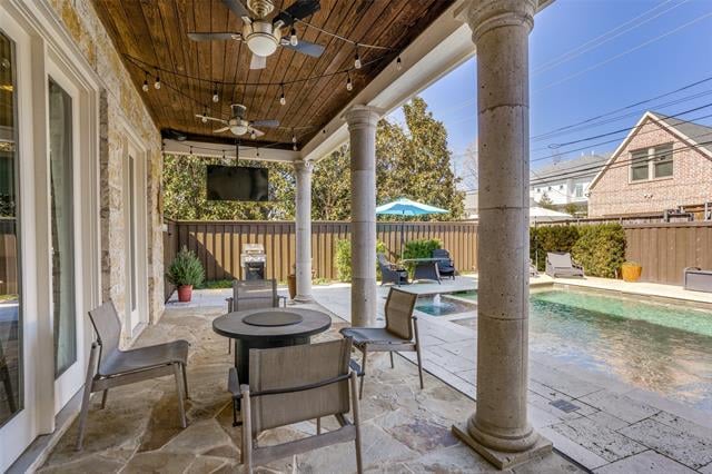 Covered stone patio with a wood ceiling and outdoor dining area beside a swimming pool.