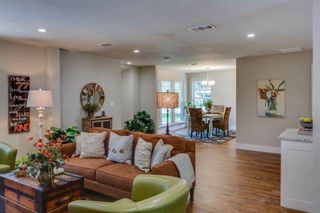 Open-plan living room with a rust-colored sectional, green chairs, hardwood floors, and dining area by the windows.