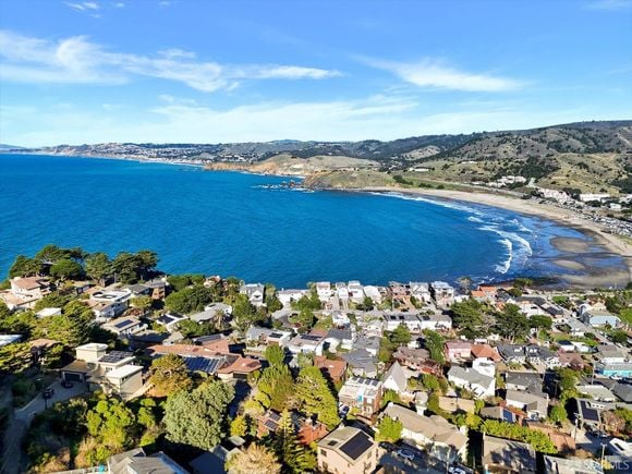 Coastal neighborhood surrounding a broad blue bay and curved shoreline.