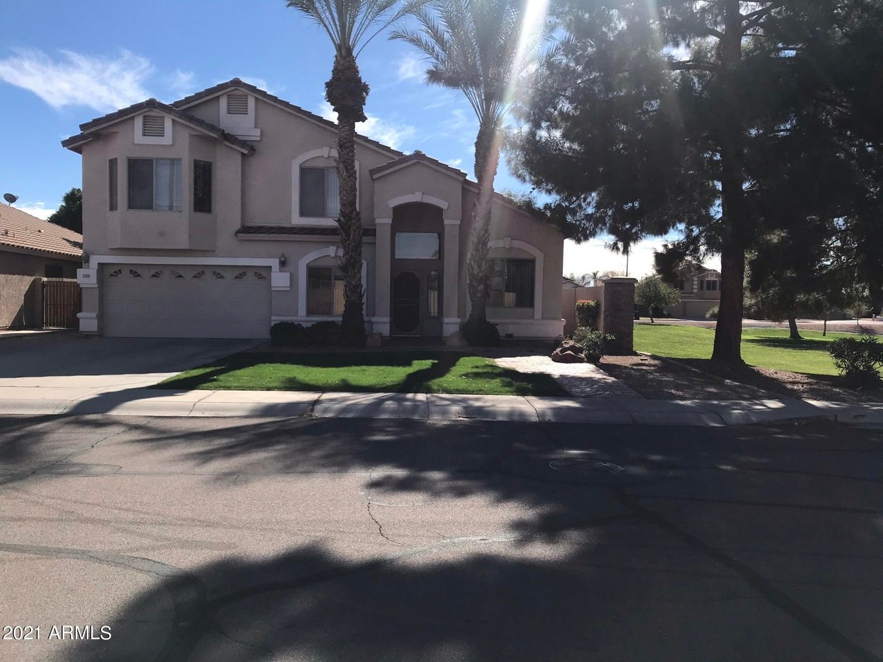 Two-story stucco house with a double garage, palm trees, and a shaded front lawn.