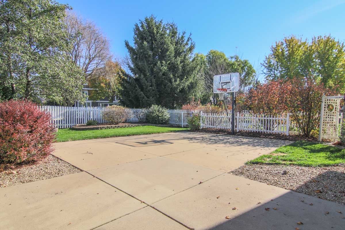 Backyard basketball court with a hoop, white picket fence, and autumn landscaping.