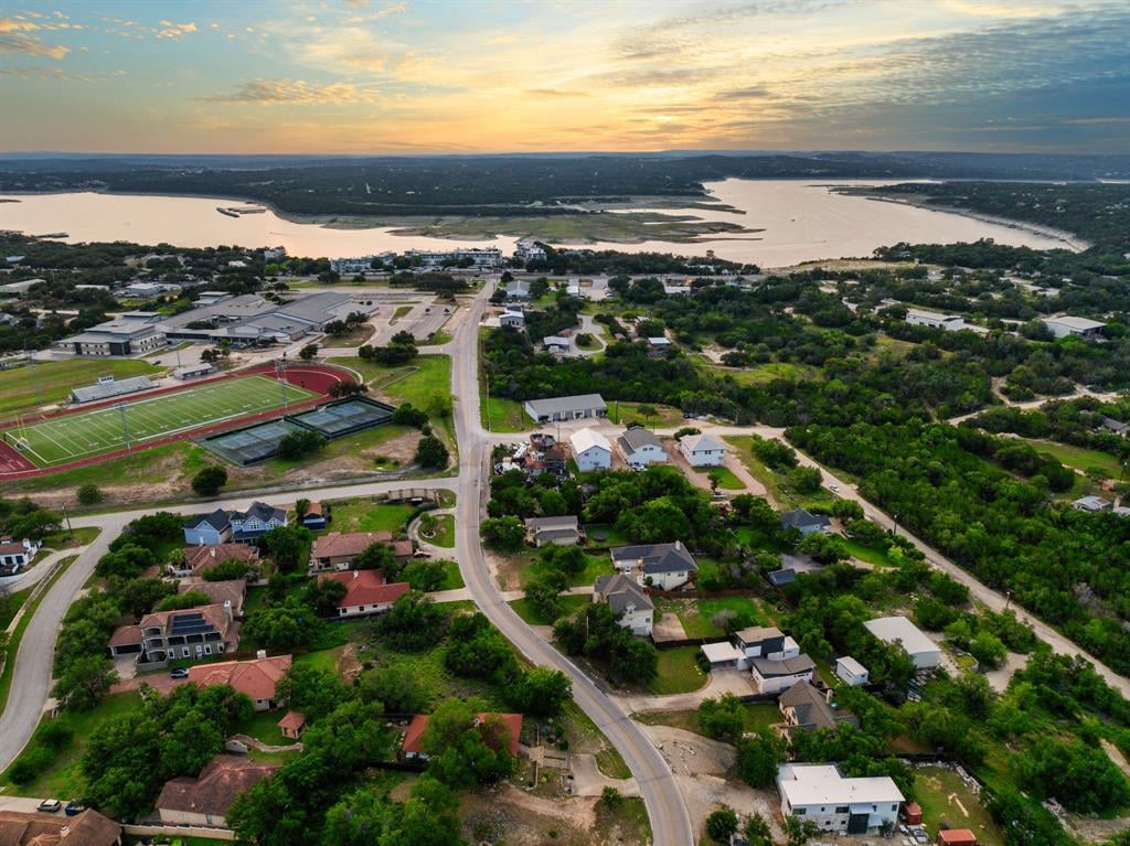 Aerial view of a lakeside neighborhood, school sports field, and winding road at sunset.