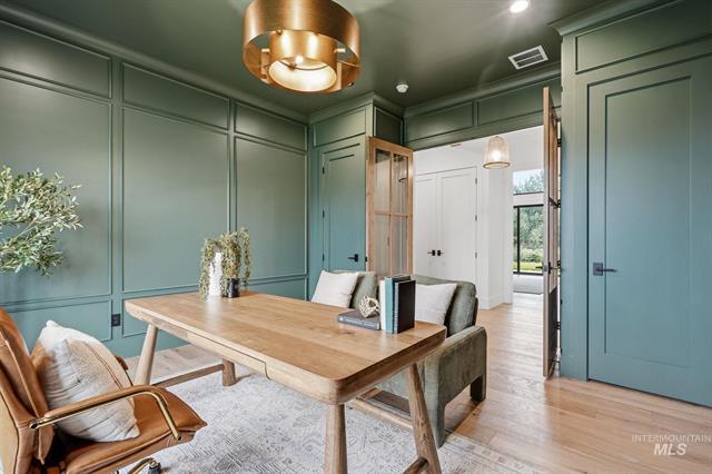 Home office with teal paneled walls, built-in cabinets, and a wood desk beneath a brass pendant light.