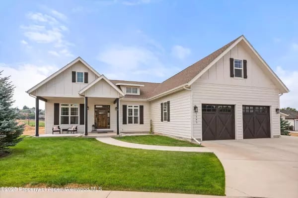 Two-story light-colored home with a covered porch, dark double garage doors, and a curved walkway across the lawn.