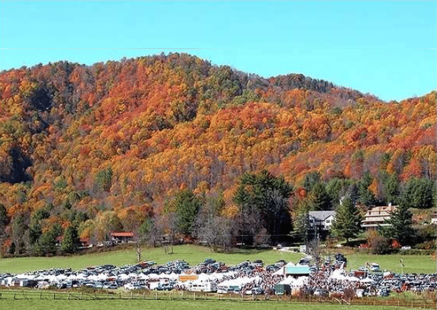 Autumn mountain ridge above a field of parked cars and event tents.