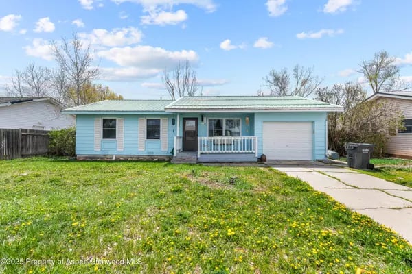 Light blue single-story house with a covered porch, attached garage, and broad grassy front yard.