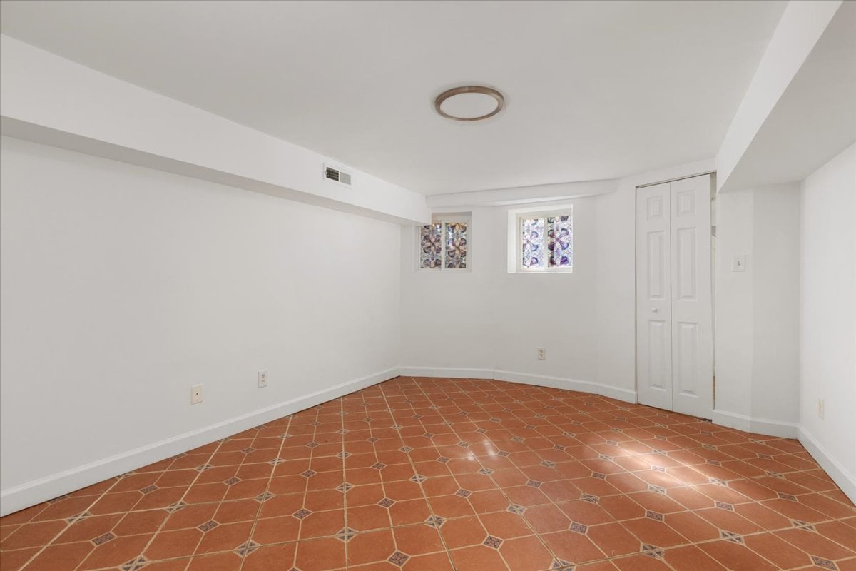 Empty room with terracotta-patterned tile floors, two small windows, and a closet.