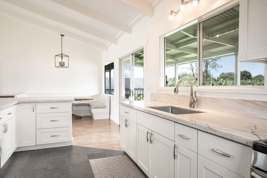 Bright white kitchen with marble counters, broad windows, and a built-in breakfast nook.