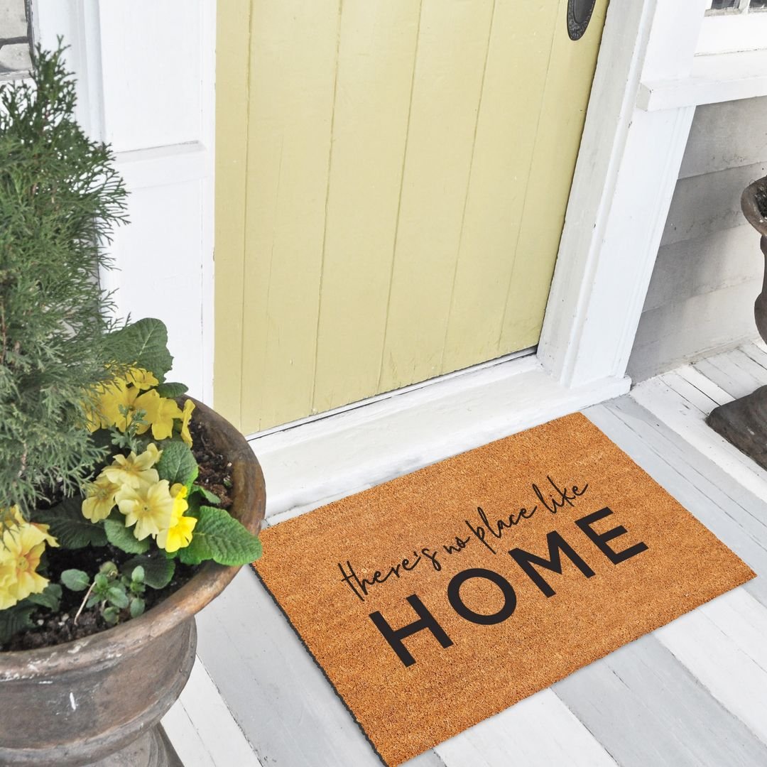 Yellow front door with a HOME doormat and a planter of yellow flowers.