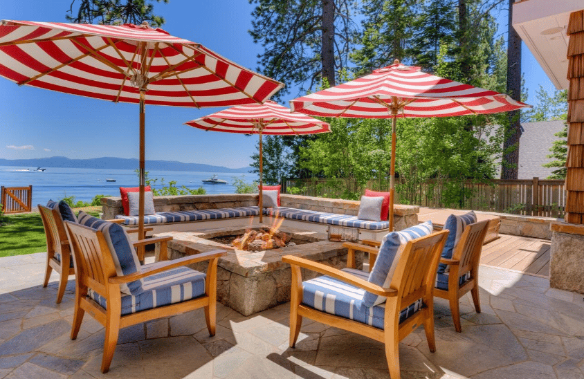 Furnished lakefront patio with striped umbrellas, a stone fire pit, and lake views.