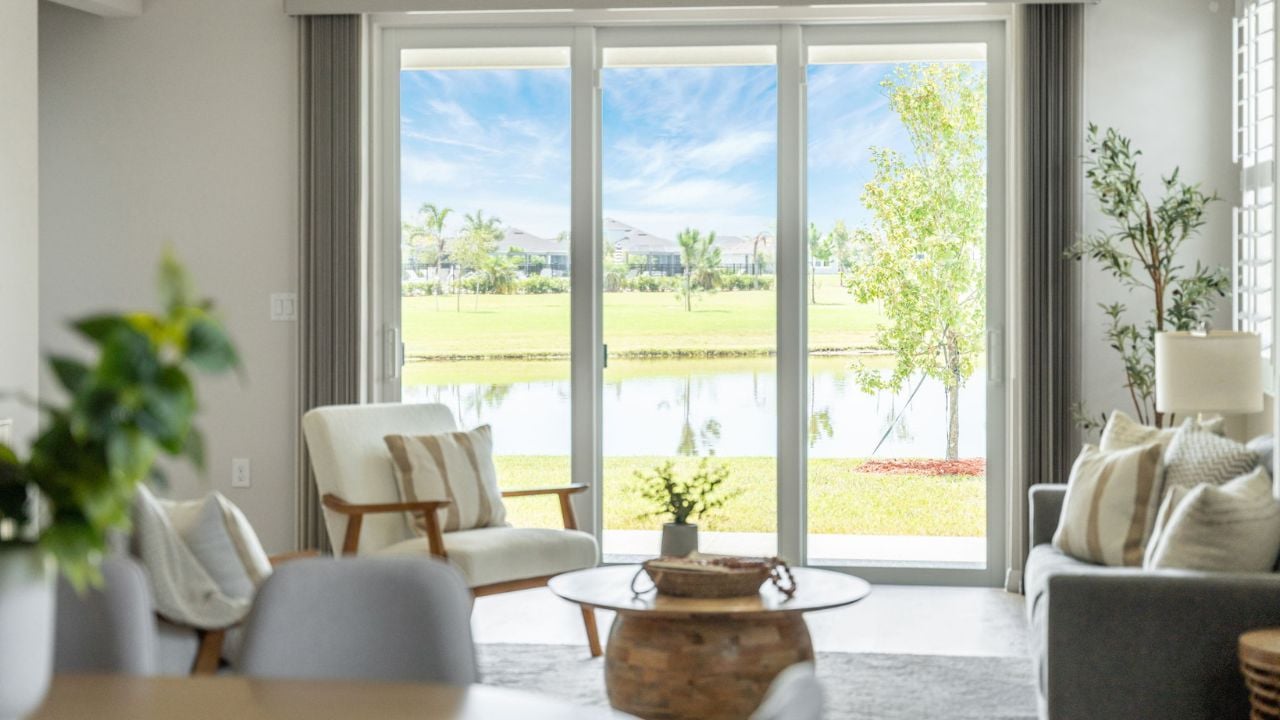 Furnished living room with large glass doors overlooking a pond and lawn.