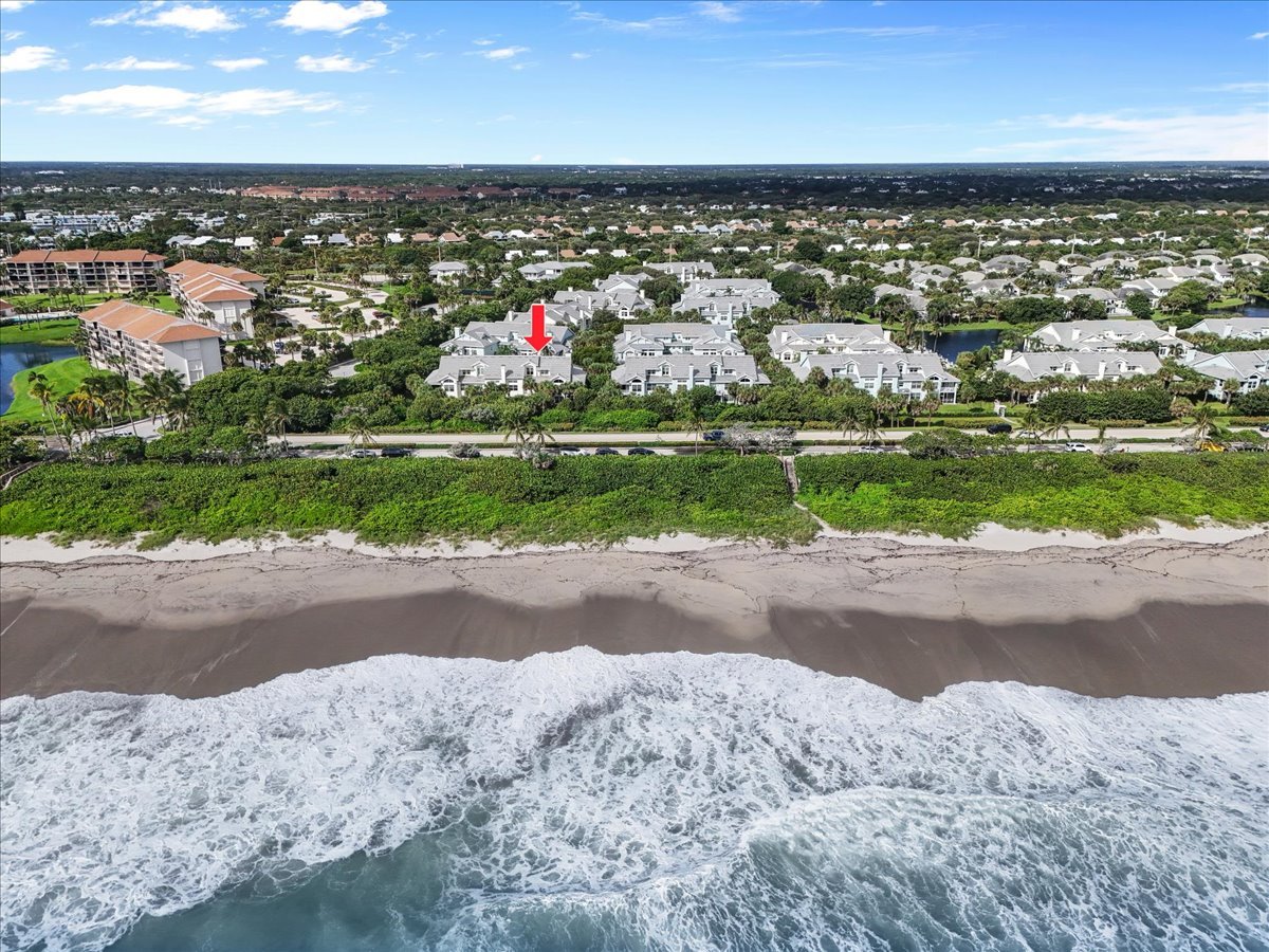 Aerial view of beachfront condominiums, with a red arrow marking the white-roofed buildings behind the shore.